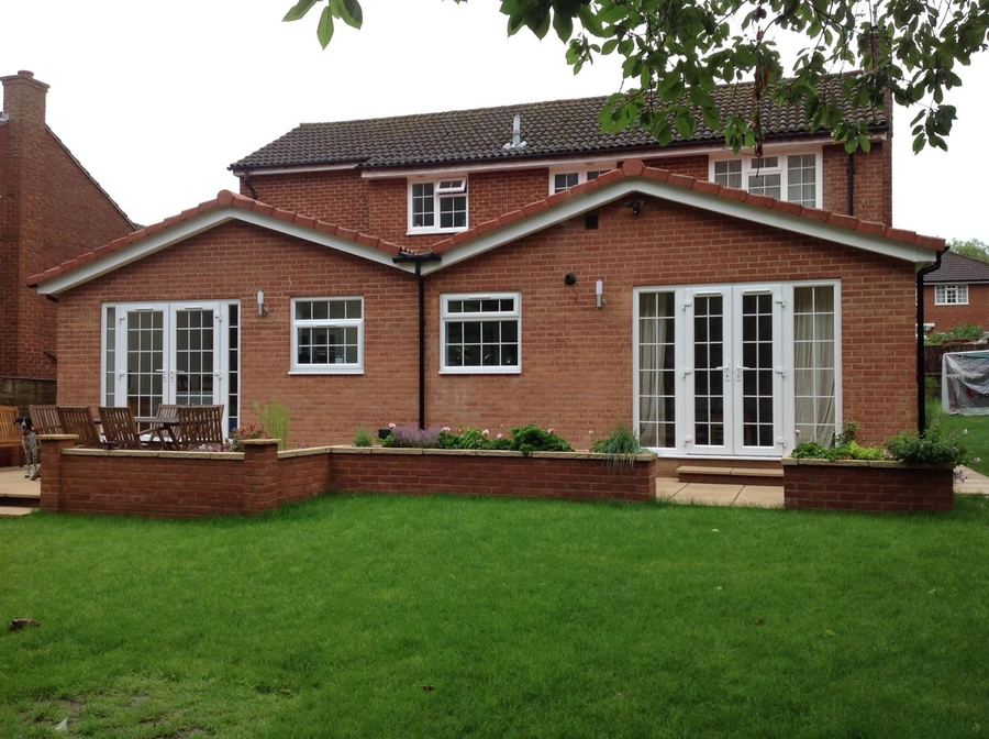 Twin gable single storey rear extension in red brick with French doors onto a lawn