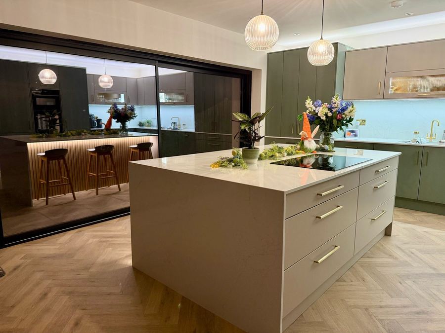Handleless kitchen in sage and taupe with a stone island and pendant lights